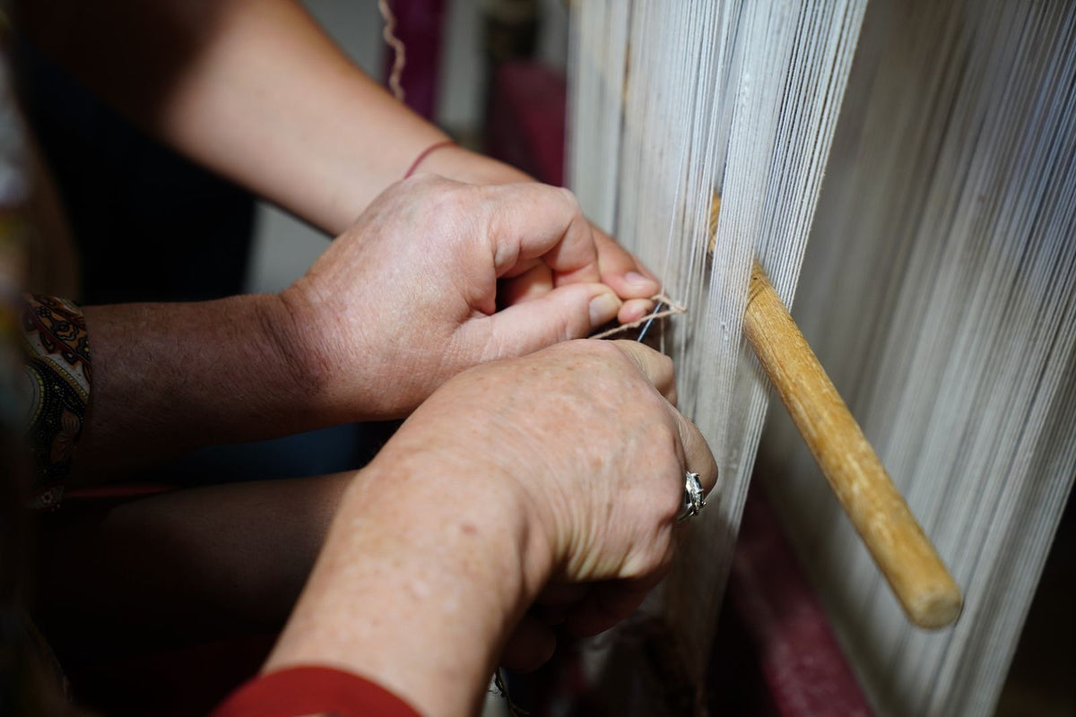 Hands weaving threads on a traditional loom